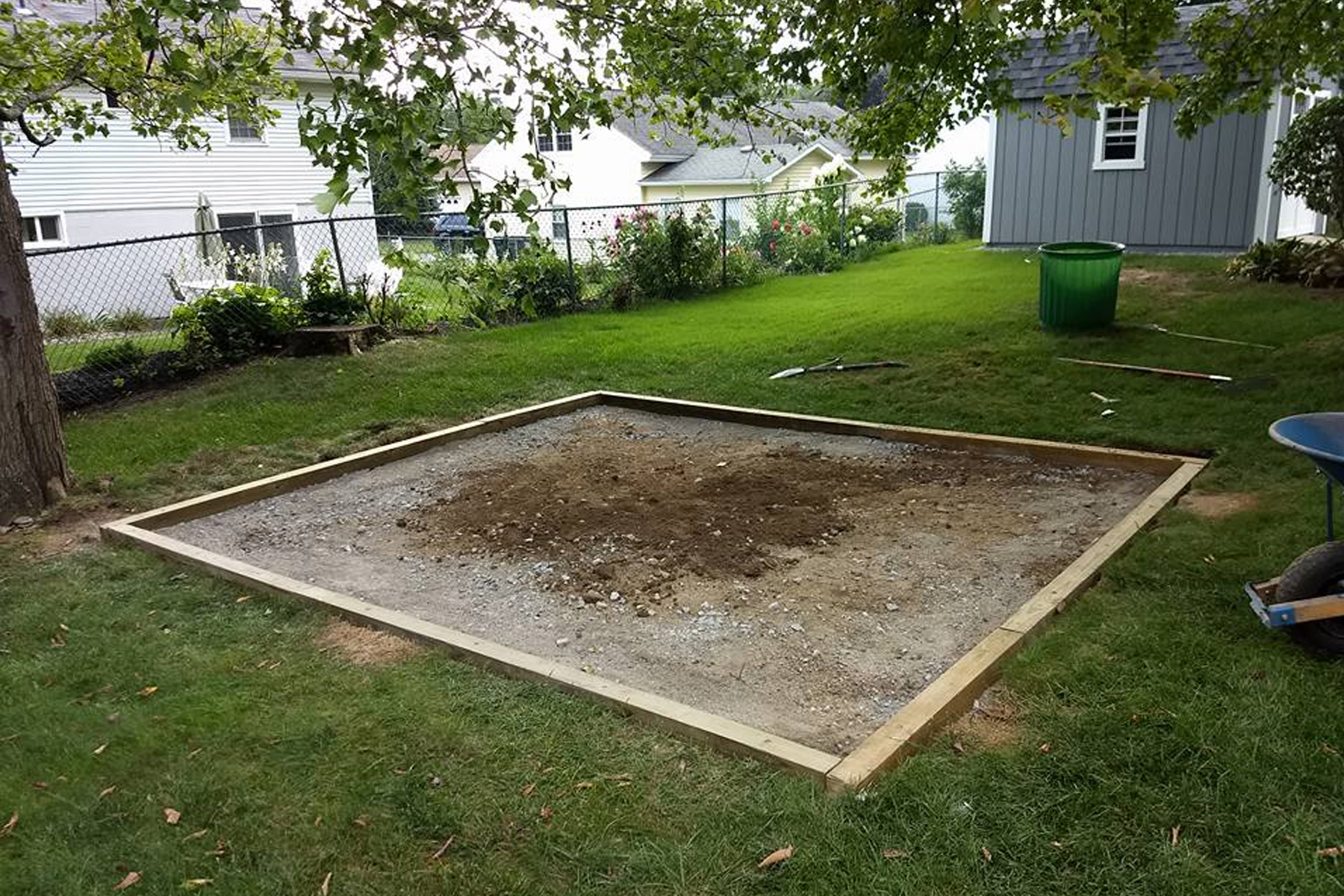 A newly framed patio area with dirt and landscaping sand being added to the center