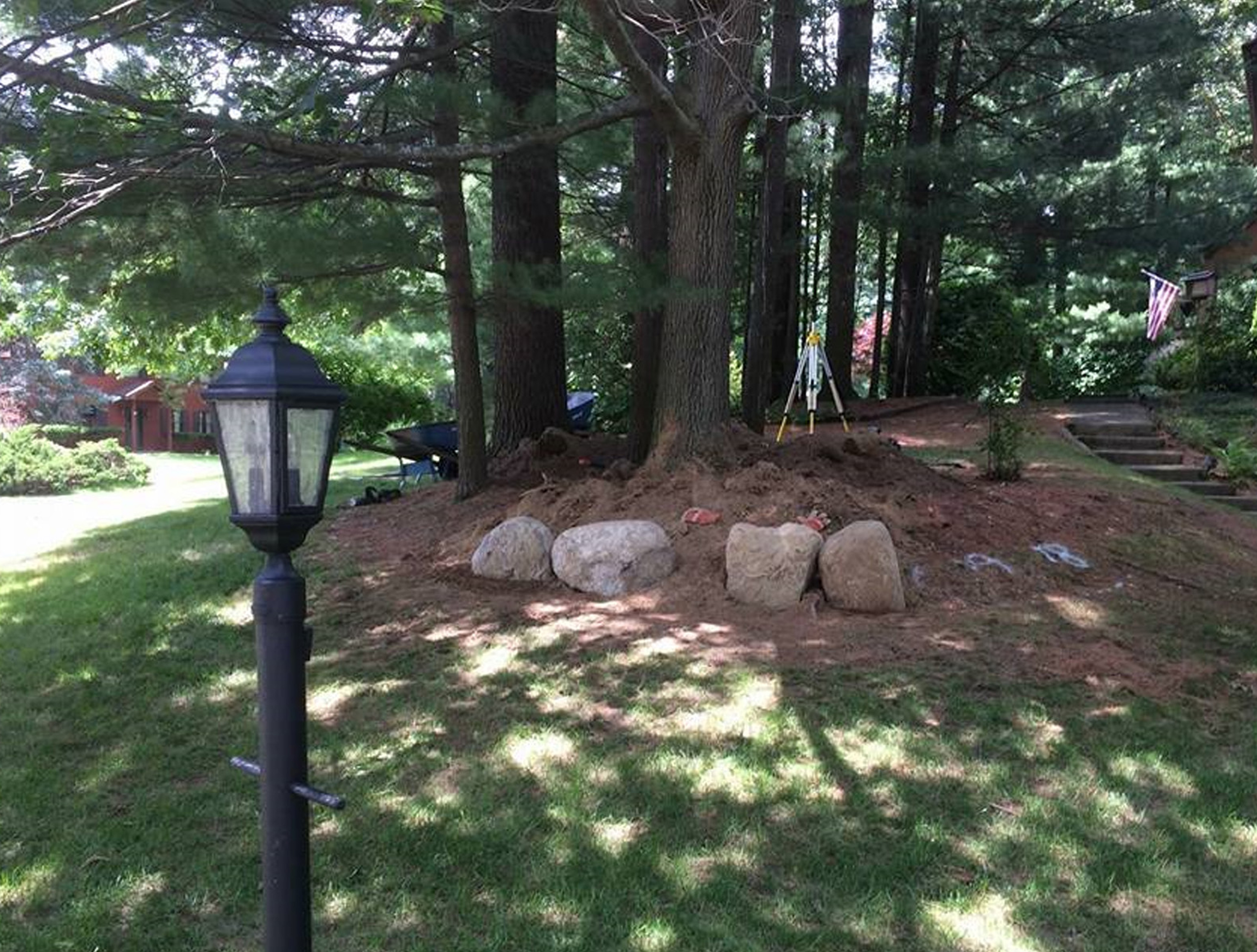 Excavation is in progress, around the trees, with some large stone placed as the start of the retaining wall