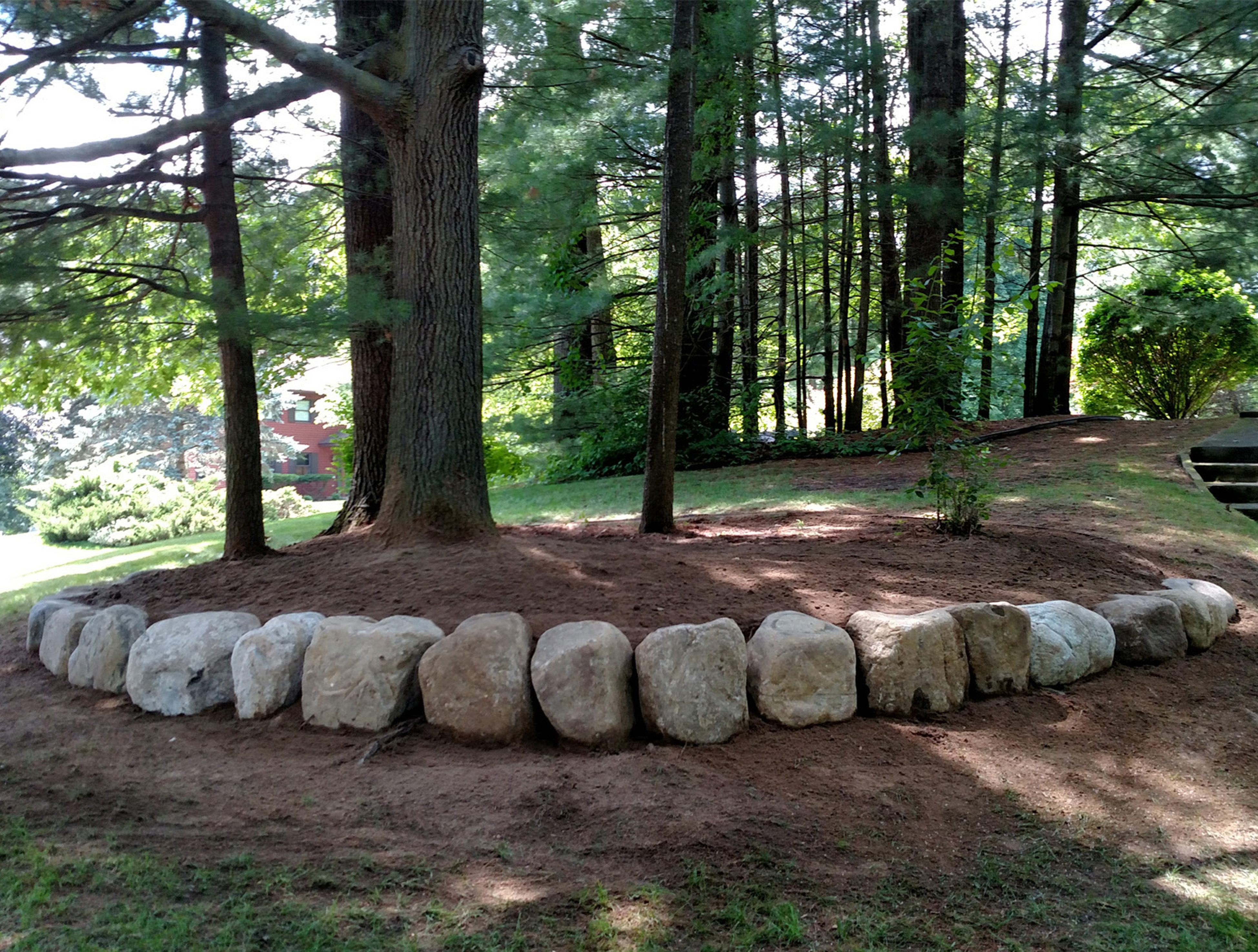 The right side of the newly leveled hill area with the remaining large stone placed for the retaining wall