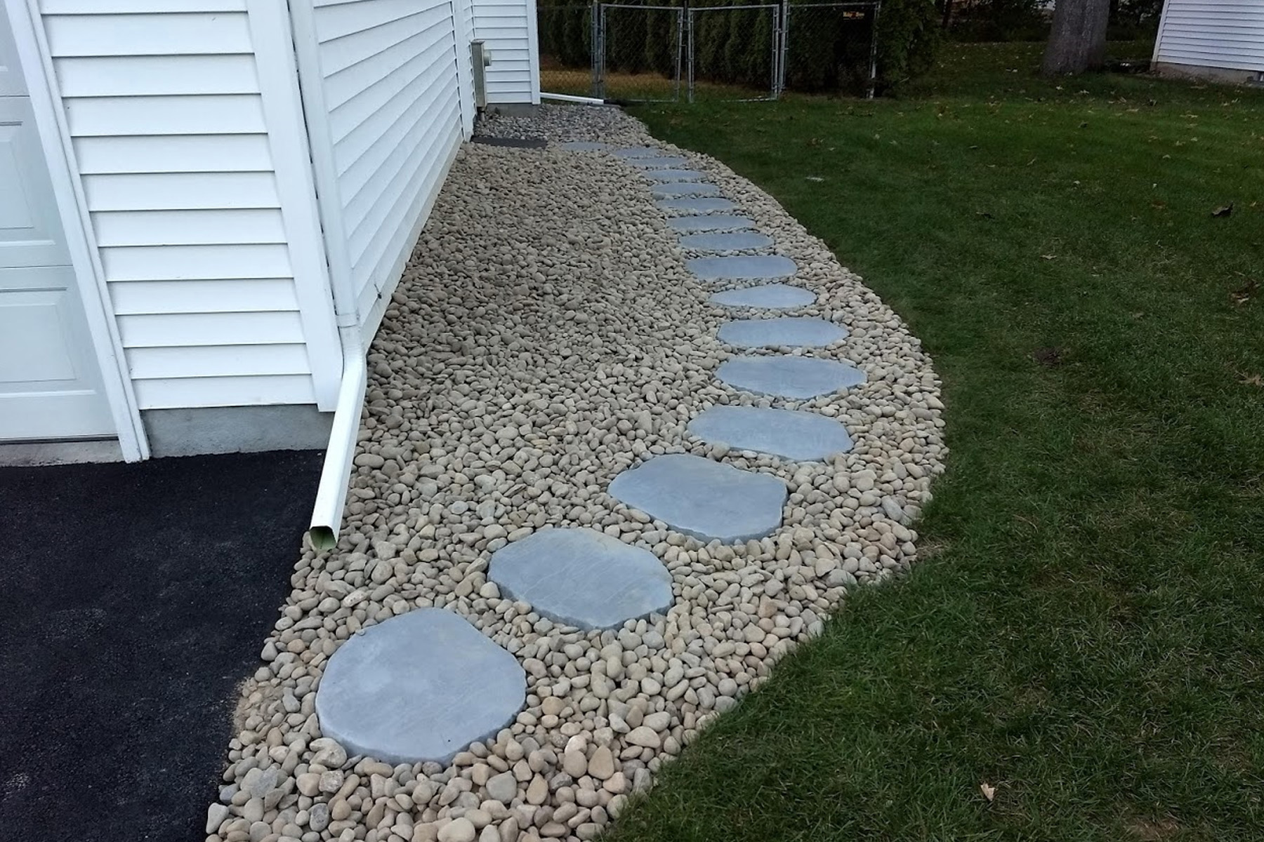The completed paver path with smooth lanscaping rocks surrounding the pavers along the side of the garage
