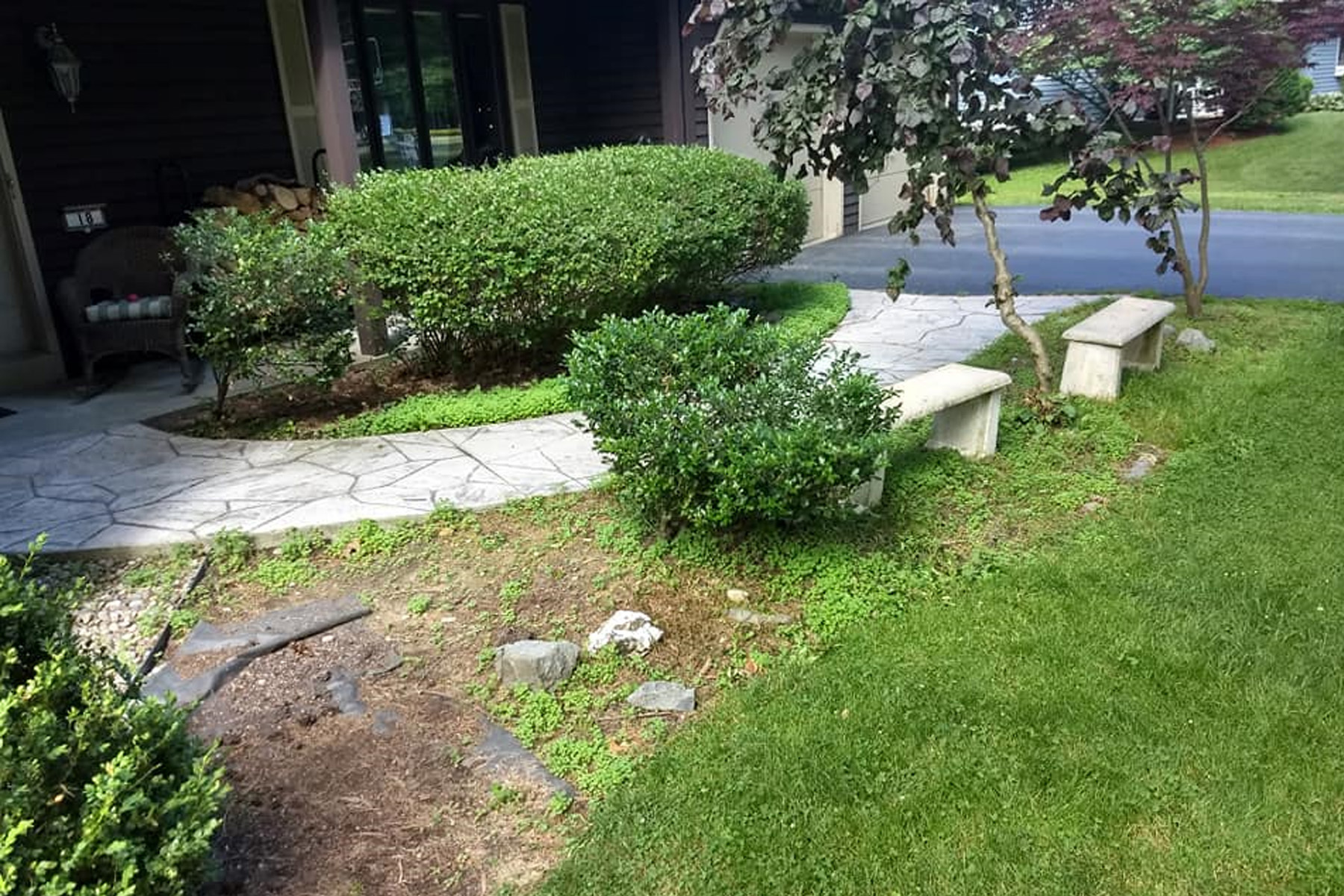 An overgrown plant bed and stone bench seating area in front of the house (bed)